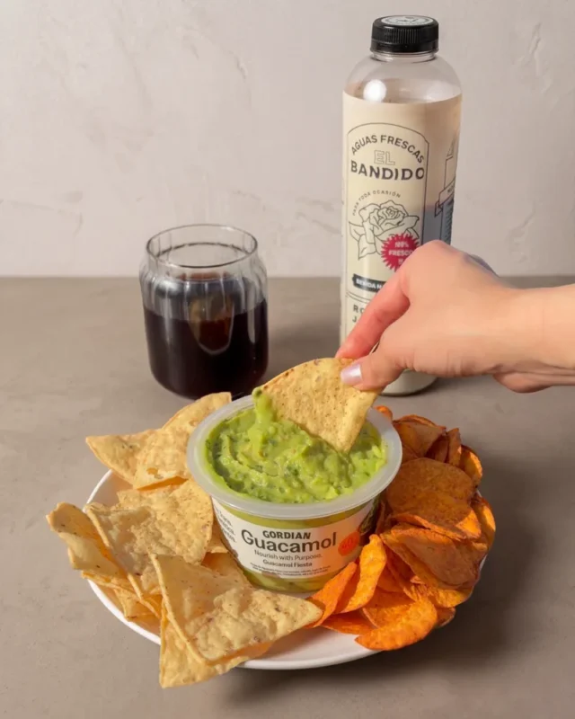 Mano tomando Guacamole Fiesta Gordian con nachos y agua de jamaica El Bandido
